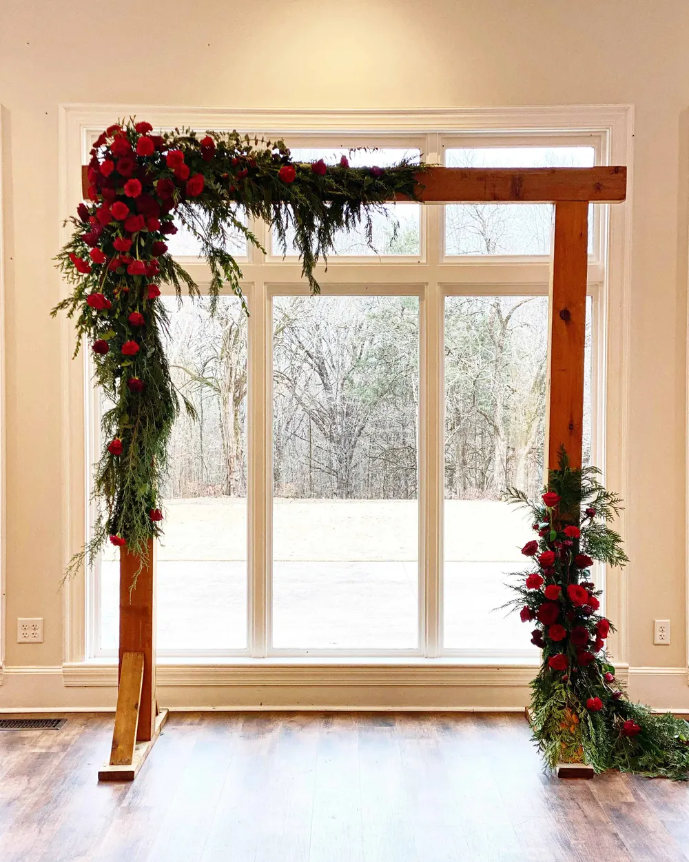 Wooden arch with red roses and evergreen in front of a window
