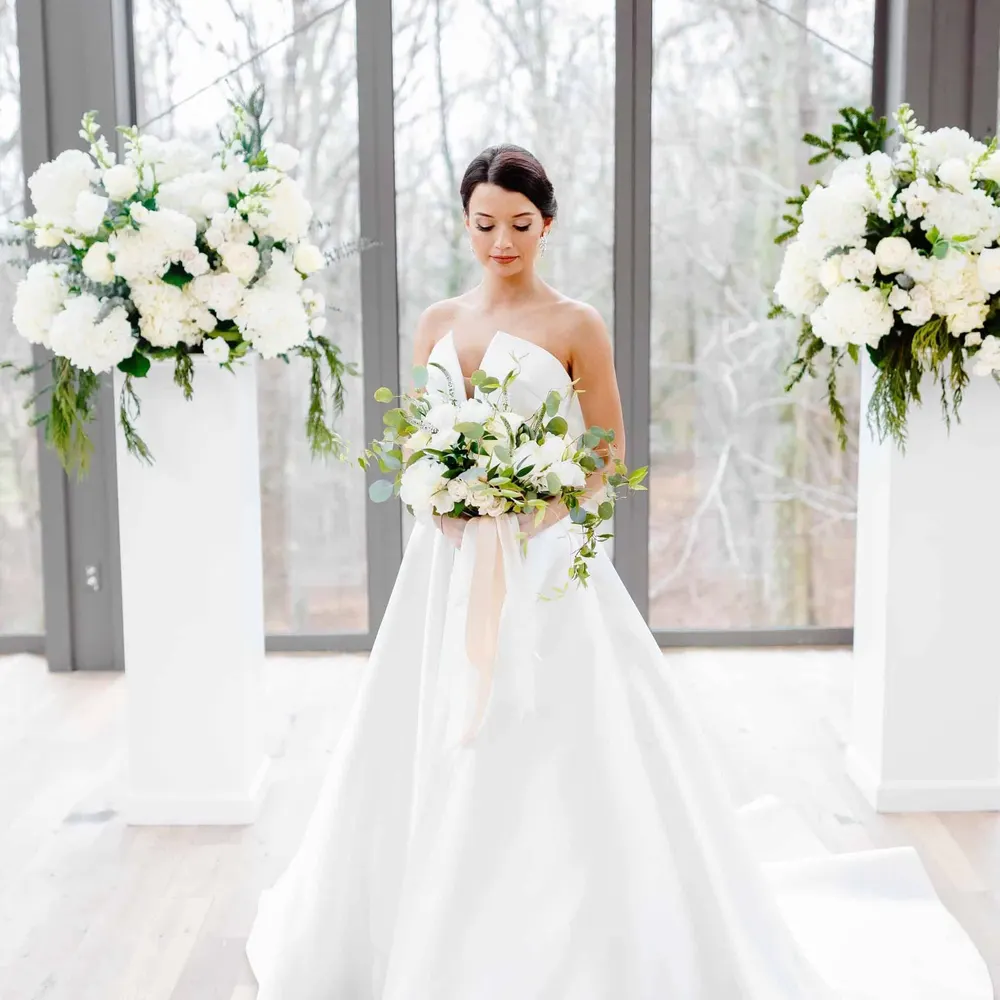 Bride holding a white and green bouquet between two pedestal arrangements