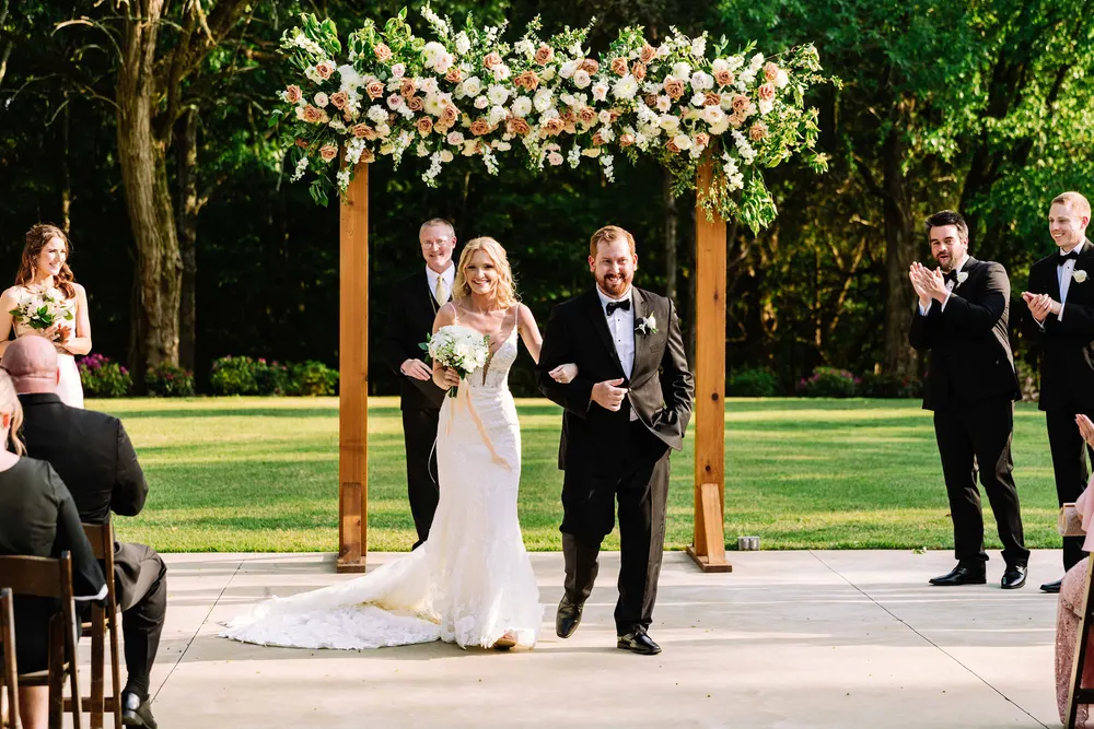 Bride and her father walking beneath a floral arch