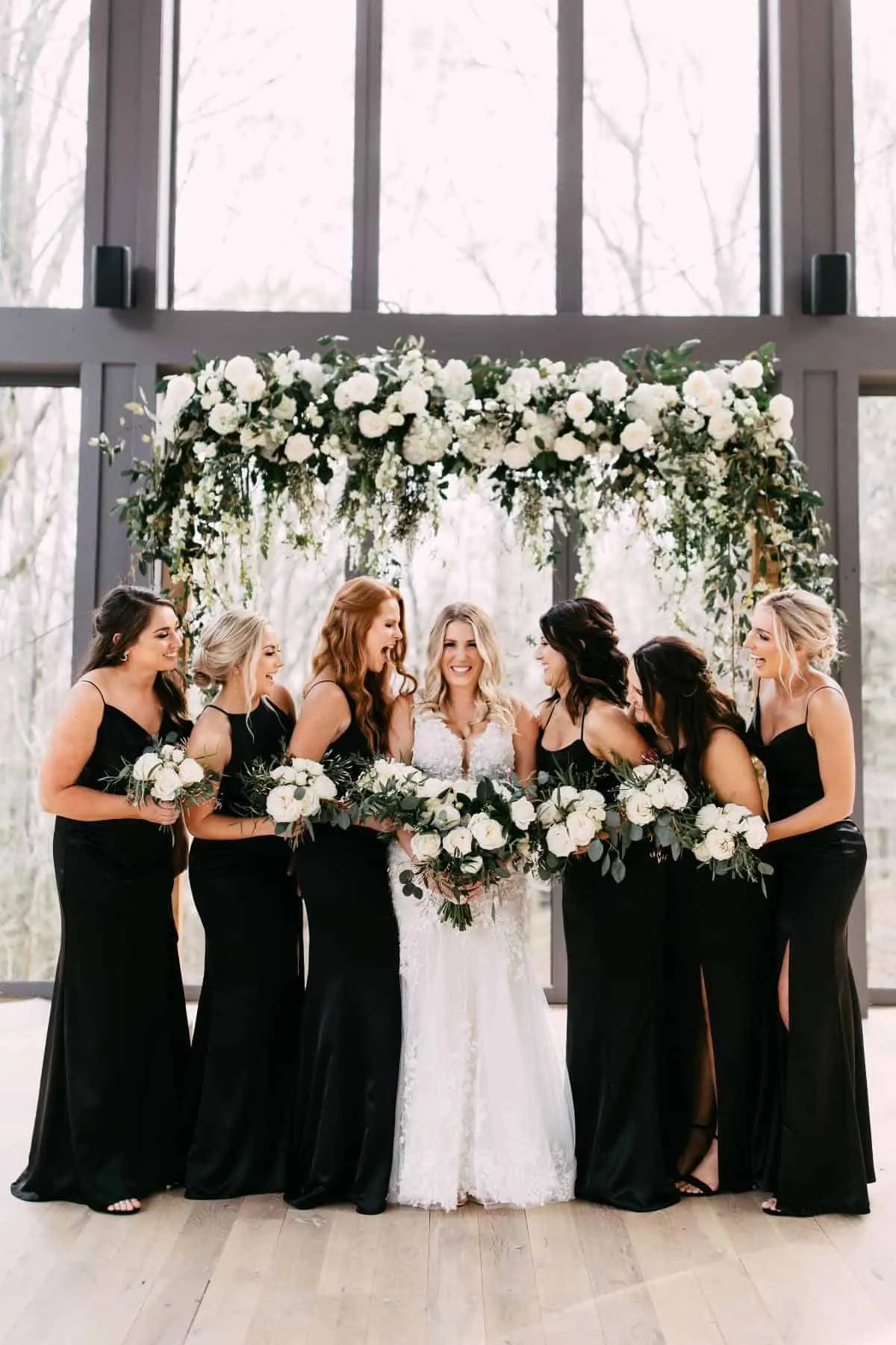Bride laughing with her bridesmaids beneath a hanging floral installation