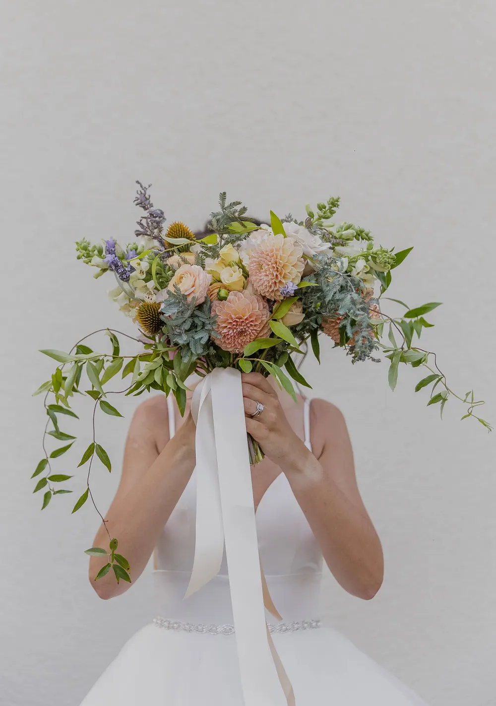 Bride holding a loose garden bouquet of peach dahlias and greenery